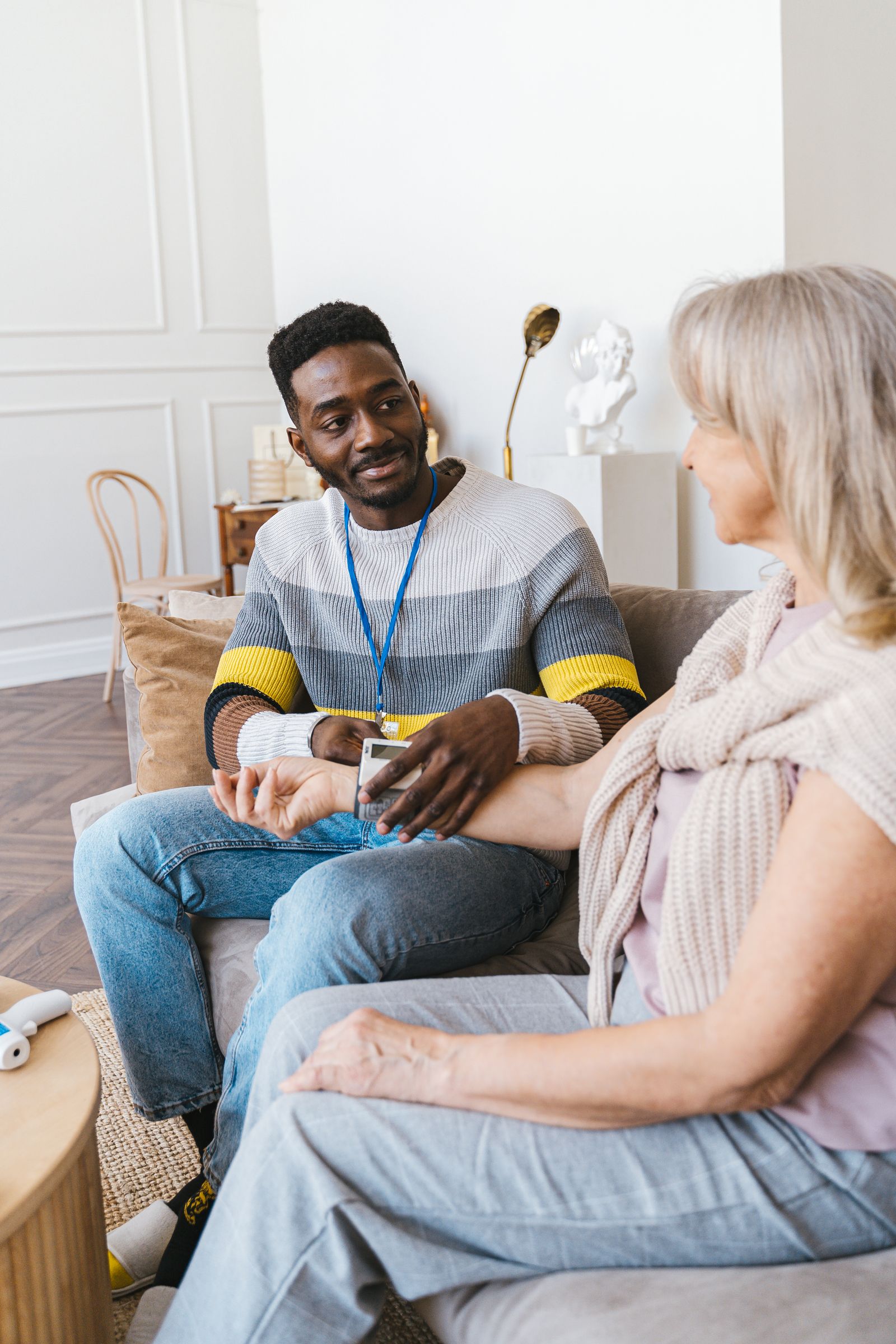 A care worker checking a patient's blood pressure at home on her couch